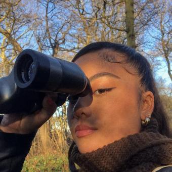 Earth Minutes event speaker, Lira Valencia, taking a selfie holding a pair of binoculars pair of